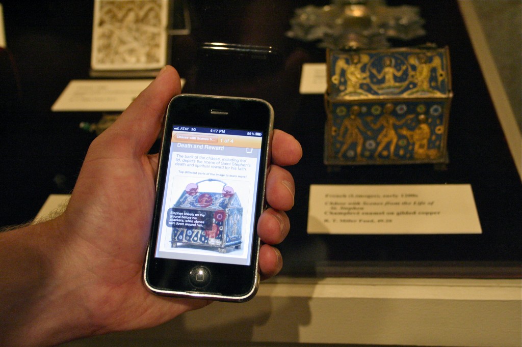 Man's hand holding an iPhone showing hotspots in the mobile app with the related artwork in the background