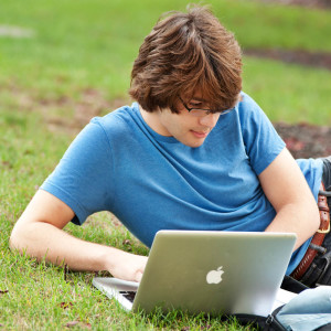 male student working on macbook outside